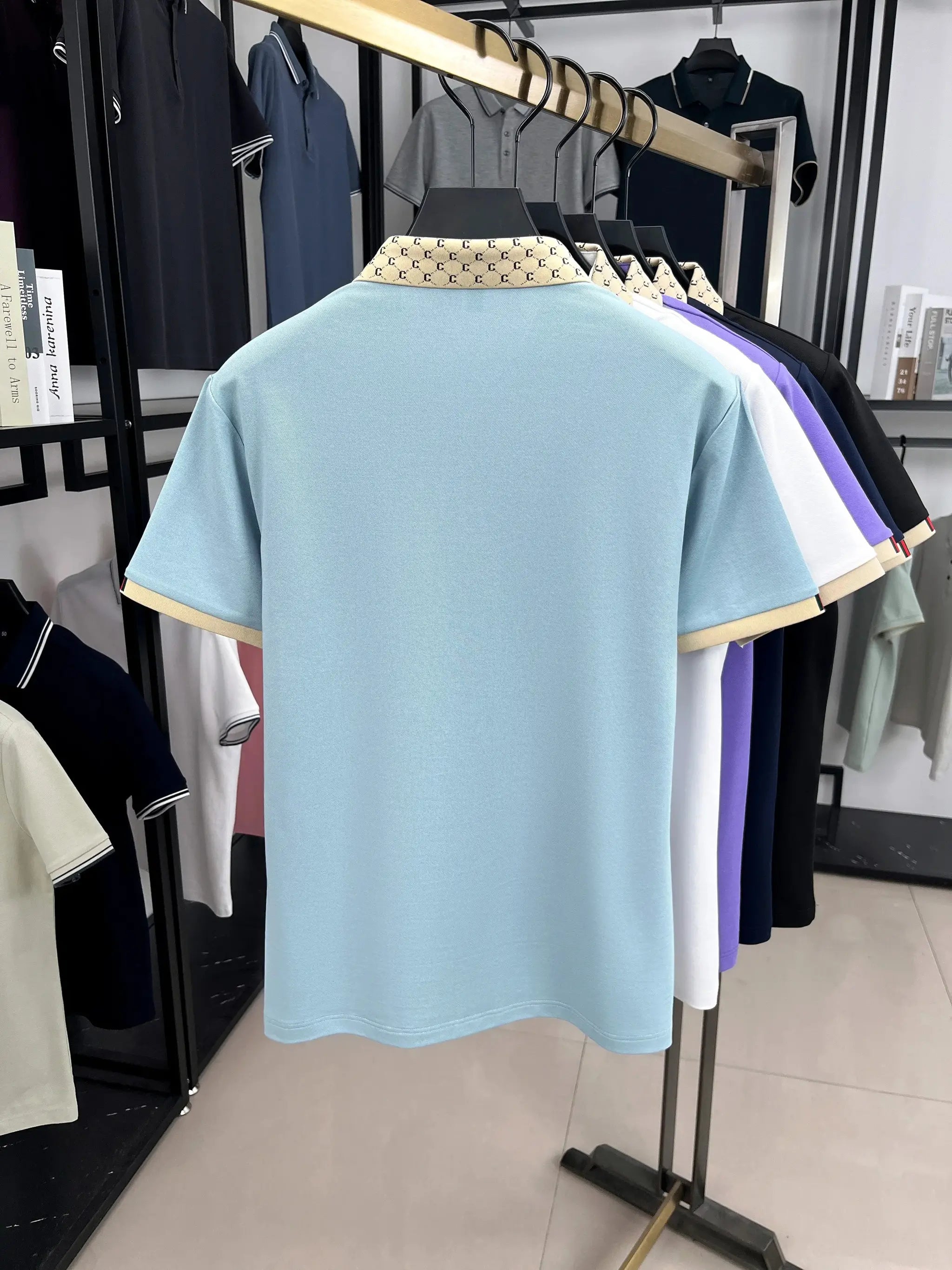 Men's light blue polo shirt with beige patterned jacquard collar; rack shows several colored polos
