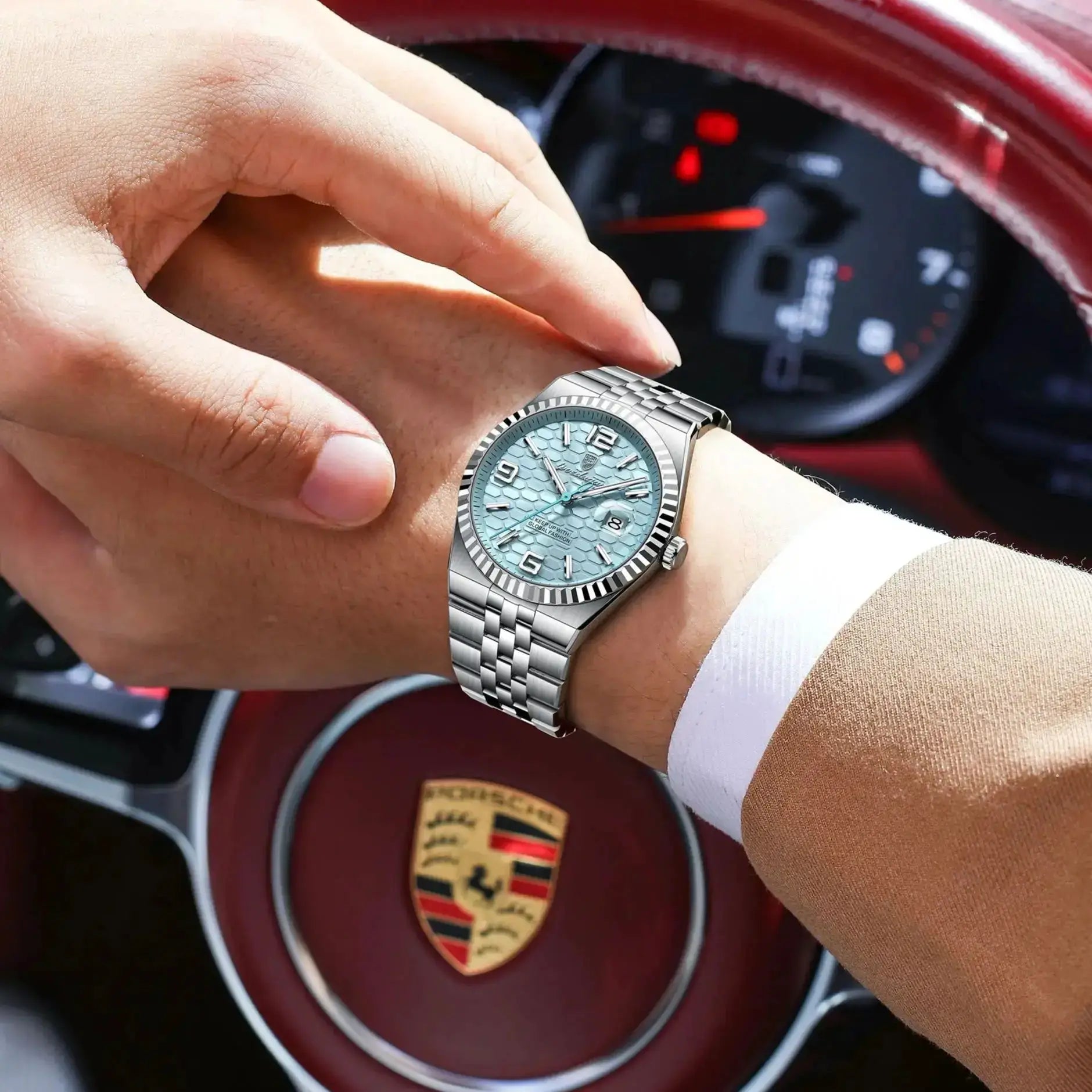 POEDAGAR stainless steel men's watch with teal textured dial and date window, on wrist near Porsche crest.