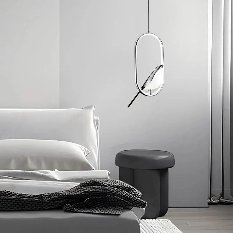 Rotatable magpie bird LED pendant light in silver finish with an oval chrome frame hanging bedside.