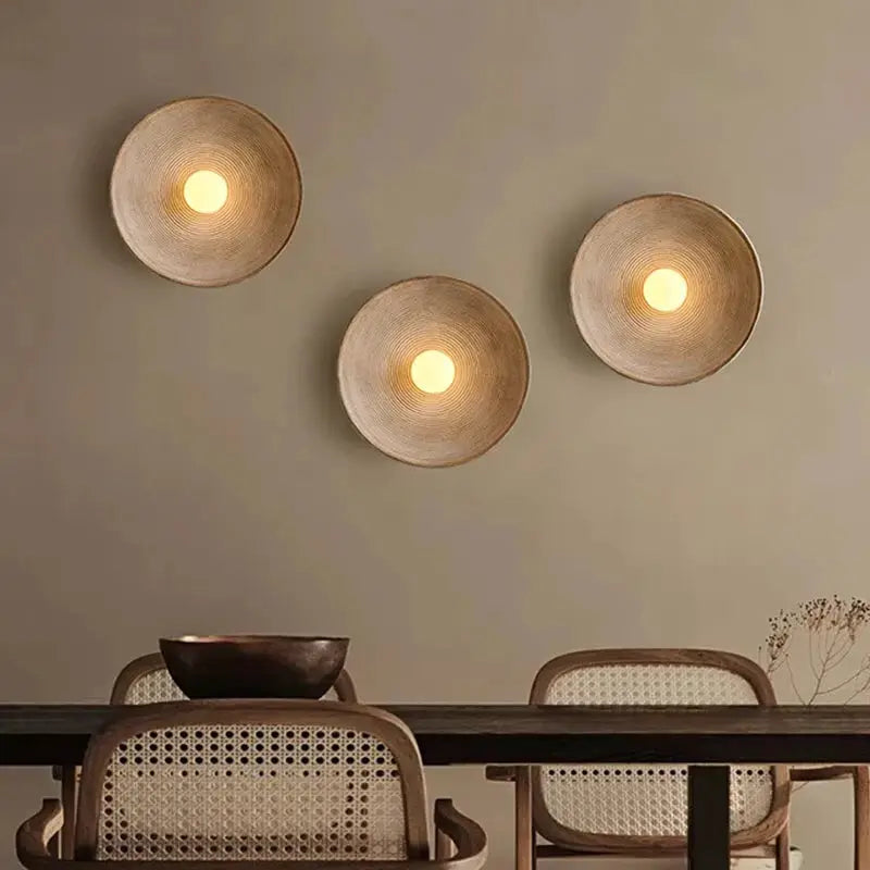Retro Japanese resin wall lamp set of three with woven beige disc shades and warm light above a dining table.