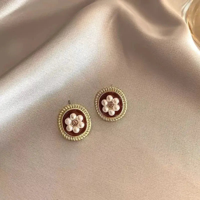 Pair of gold-tone round stud earrings with wine-red enamel center and pearl flower accents.