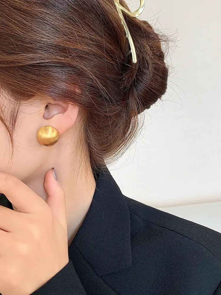 Stud earring in gold-tone brushed metal on ear with round button design