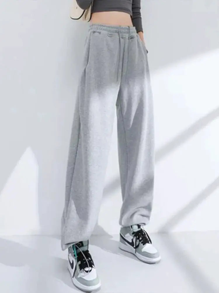 Grey sweatpants with elastic waistband, loose fit, paired with sneakers.