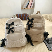 Two beige corduroy backpacks with black bow accents and front pockets
