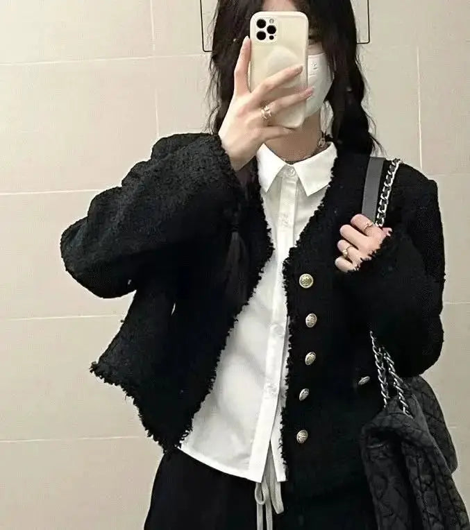 White button-down shirt with long sleeves, black textured cardigan with gold buttons and a black quilted bag.