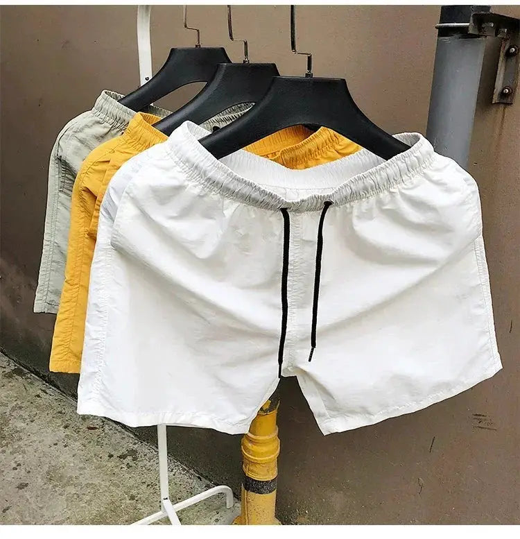 Men's swim shorts on hangers; white with black drawstring plus yellow and gray colorways