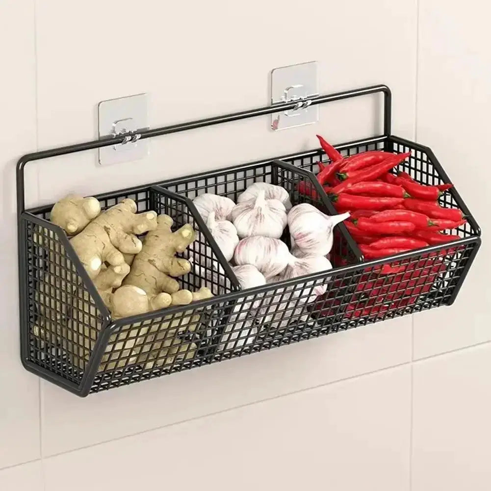 Wall-mounted black metal wire storage basket with three compartments for ginger, garlic, and red peppers