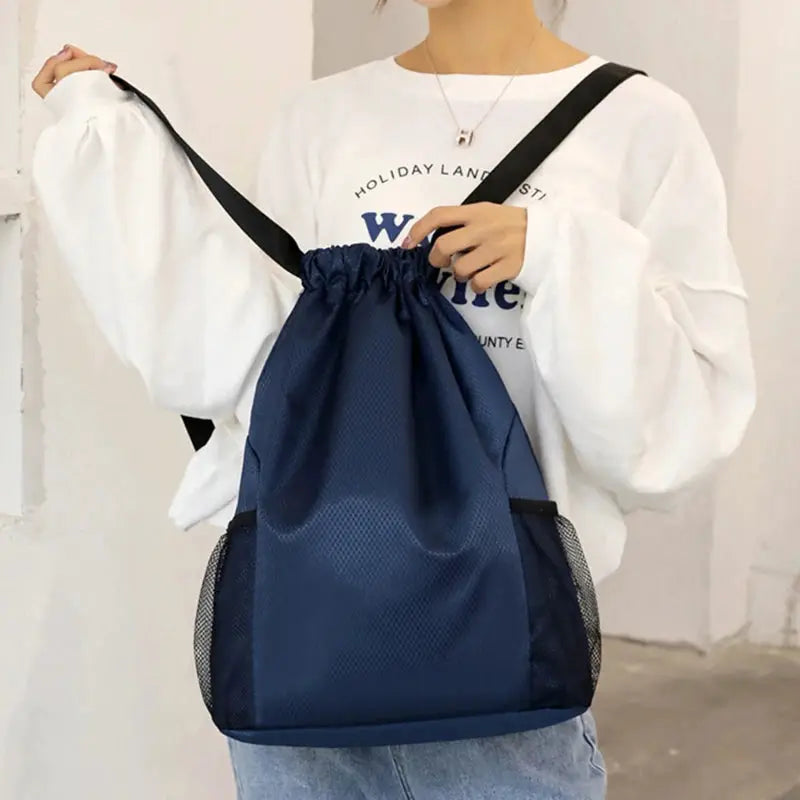 Navy blue large-capacity drawstring backpack with mesh side pockets, worn by a model in a white oversized top.