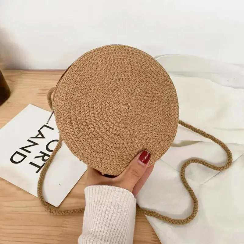 Minimalist round straw crossbody bag in beige with a long woven strap.