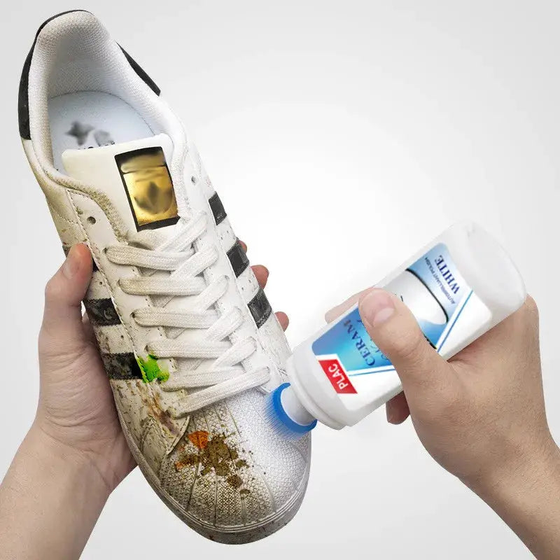 White shoe cleaner for leather sneakers; hands apply blue-capped bottle to dirty white shoe.