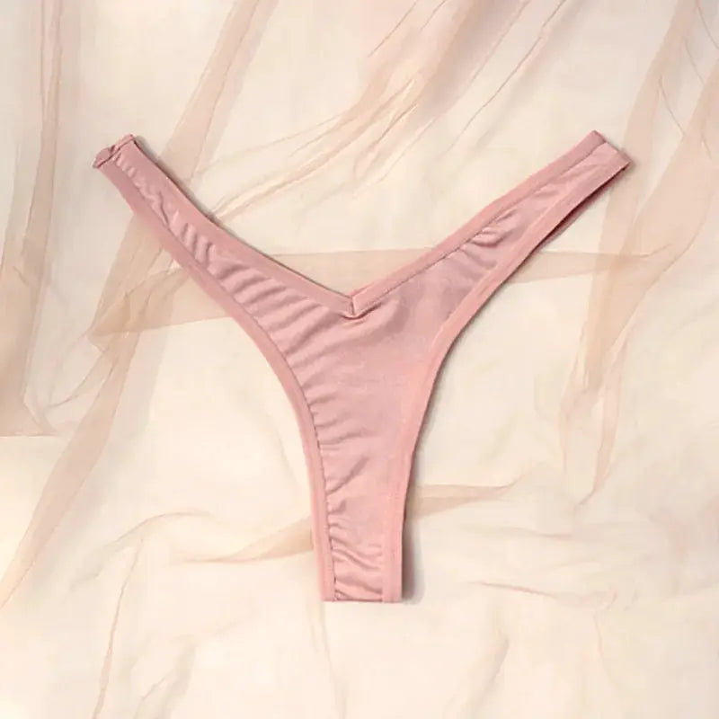 Pink low-rise thong underwear for women on soft pink fabric, simple sleek silhouette