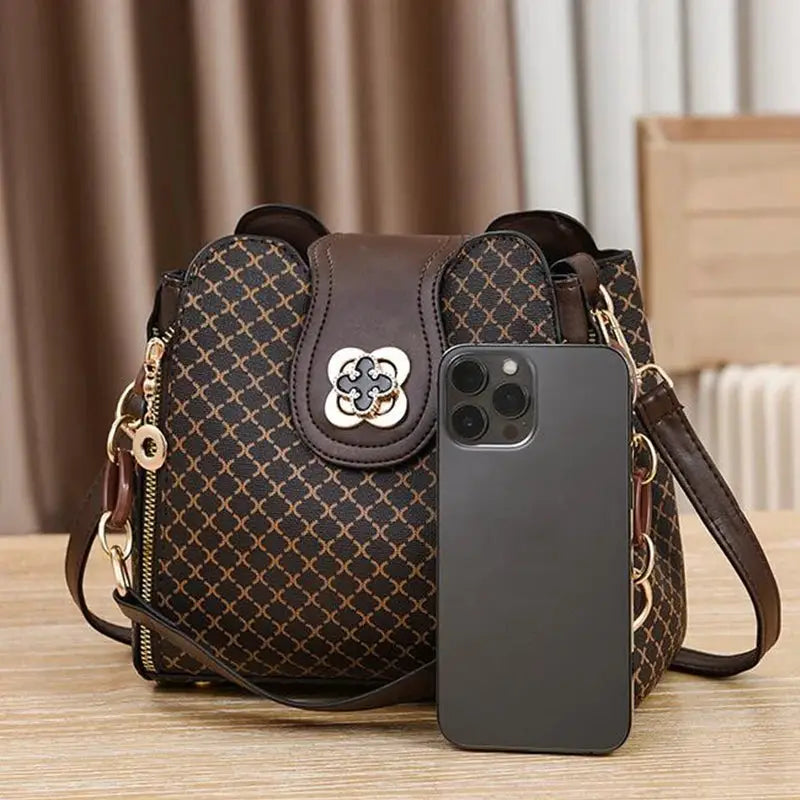 Brown flip-check print bucket bag with gold hardware, shoulder strap, and front flower emblem; large capacity.