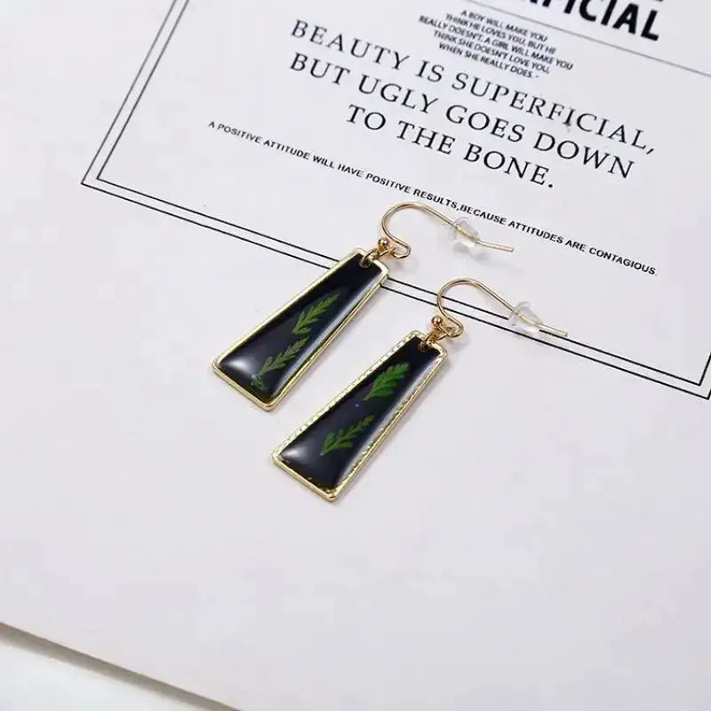 Simples Market pressed flower earrings, epoxy resin with black background and green leaves, gold-tone frame, pair