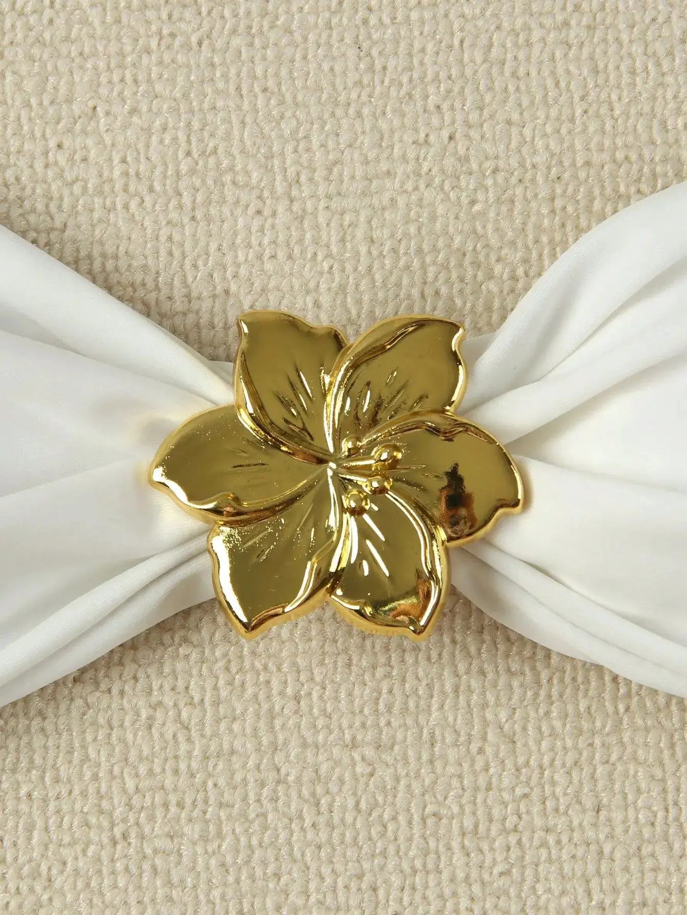 Gold floral bikini embellishment on white fabric, set against a beige carpet background