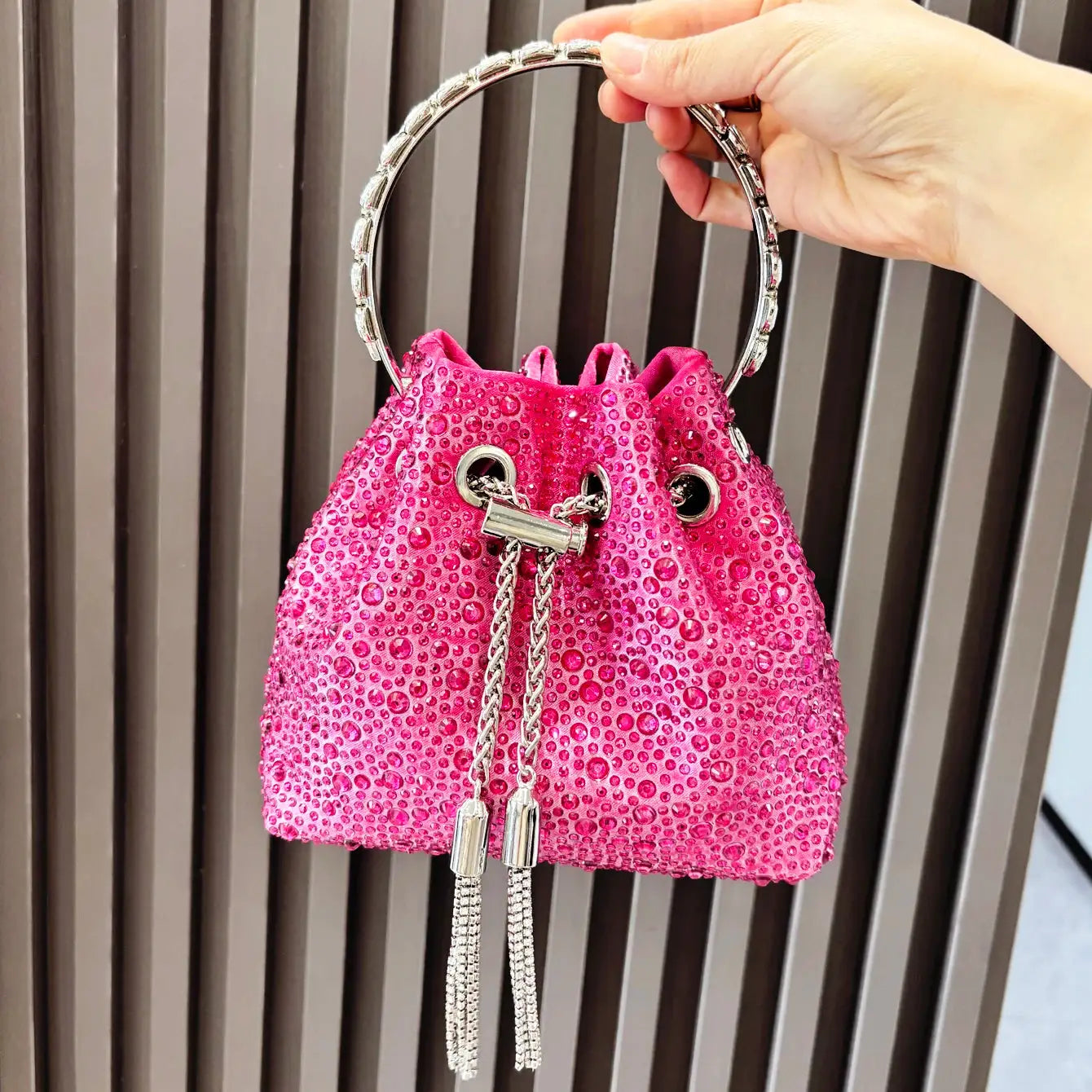 Pink rhinestone bucket-style clutch bag with silver ring handle and tassel accents