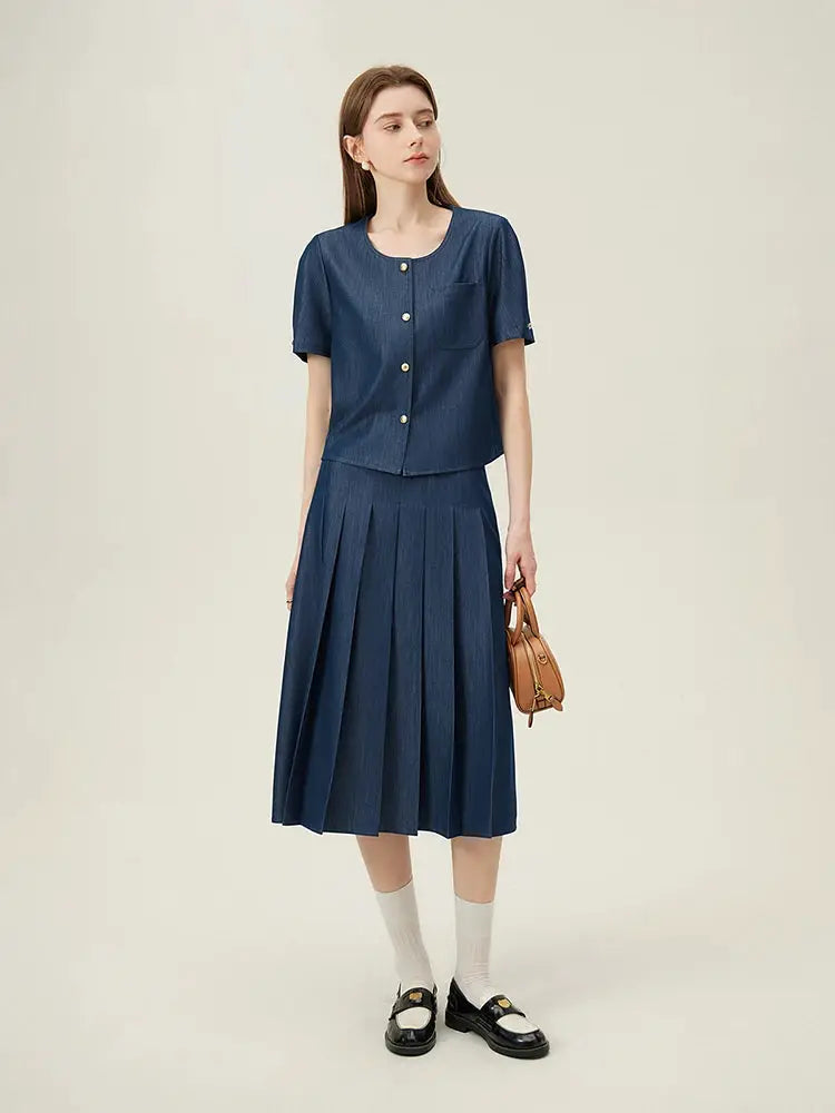 Women’s navy blue pleated long skirt with denim top, brown handbag, and black loafers.