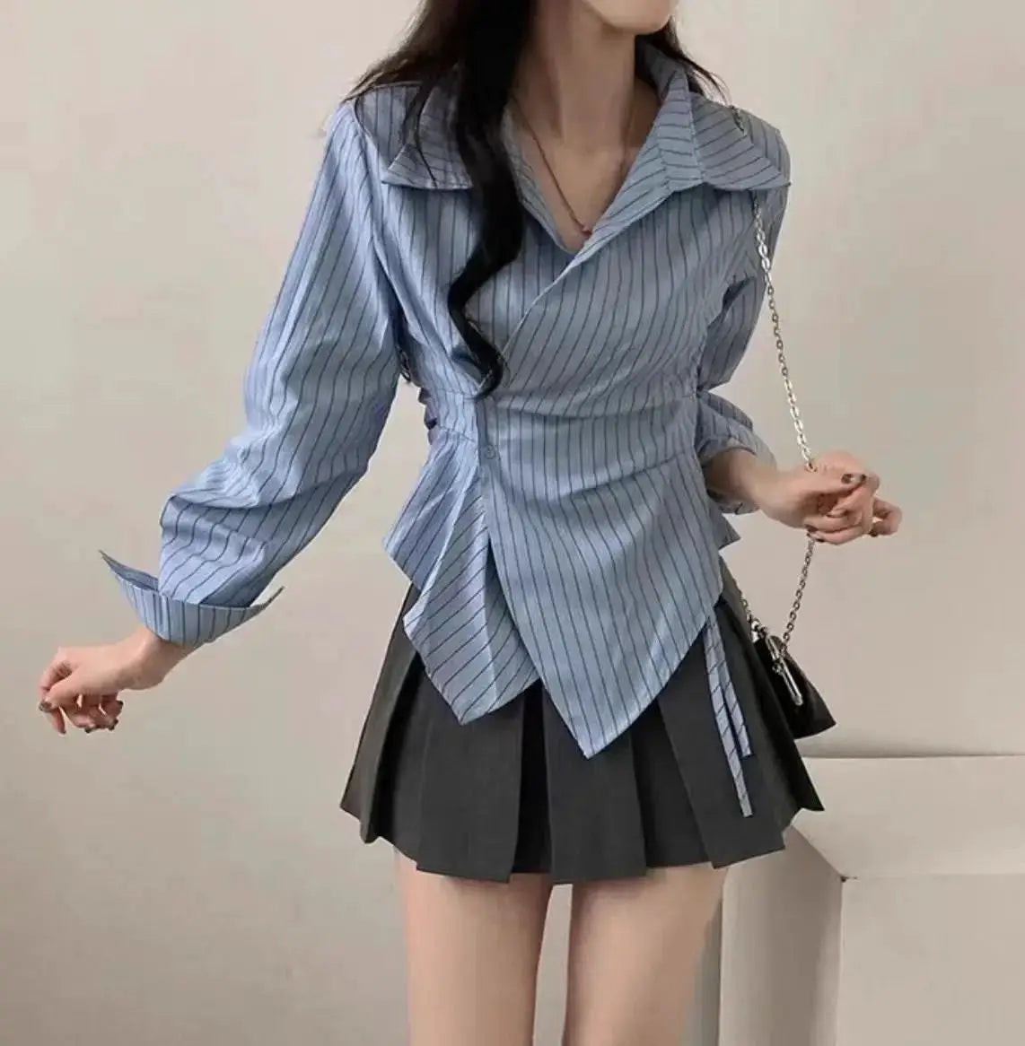 Simples Market women's blue striped long-sleeve blouse with wrap waist, paired with a pleated black mini skirt.