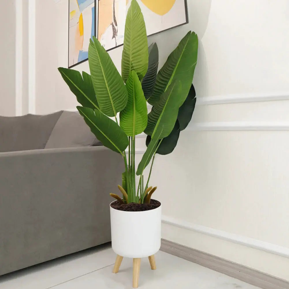 Floor-standing white round planter with wooden legs housing a green leafy plant, self-watering drainage system.