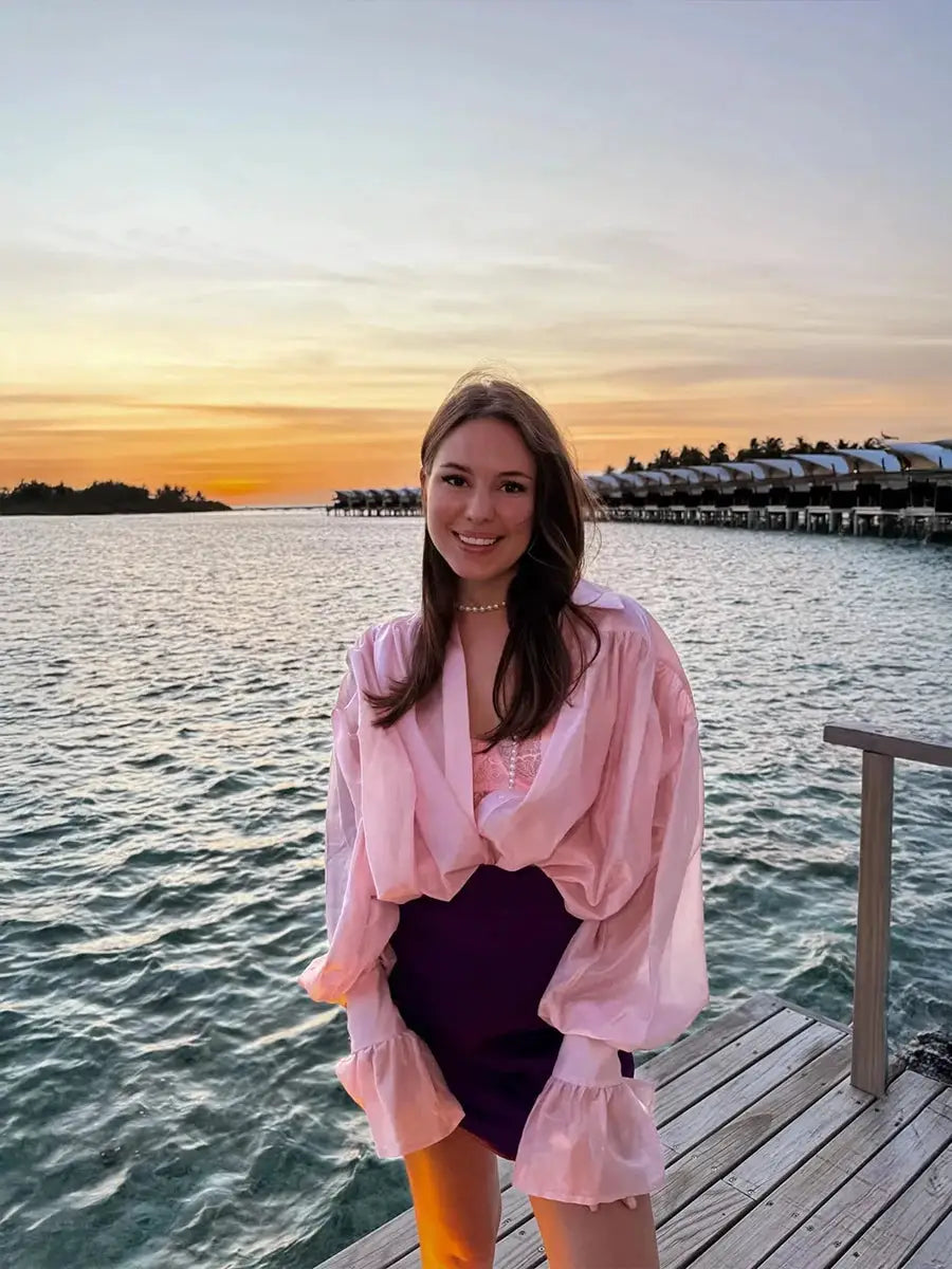 Bornladies pink loose collared shirt with flare sleeves worn by a woman on a sunset seaside dock