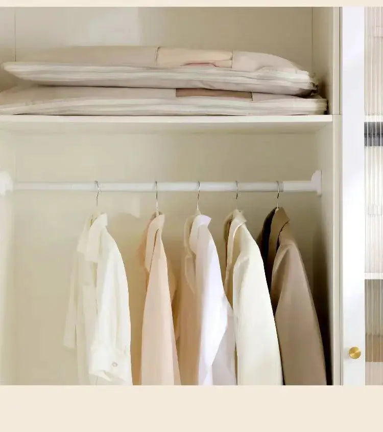 Clothing compression bag wardrobe organizer in a white closet; jackets hang on a rod with folded storage bags on the top shelf.