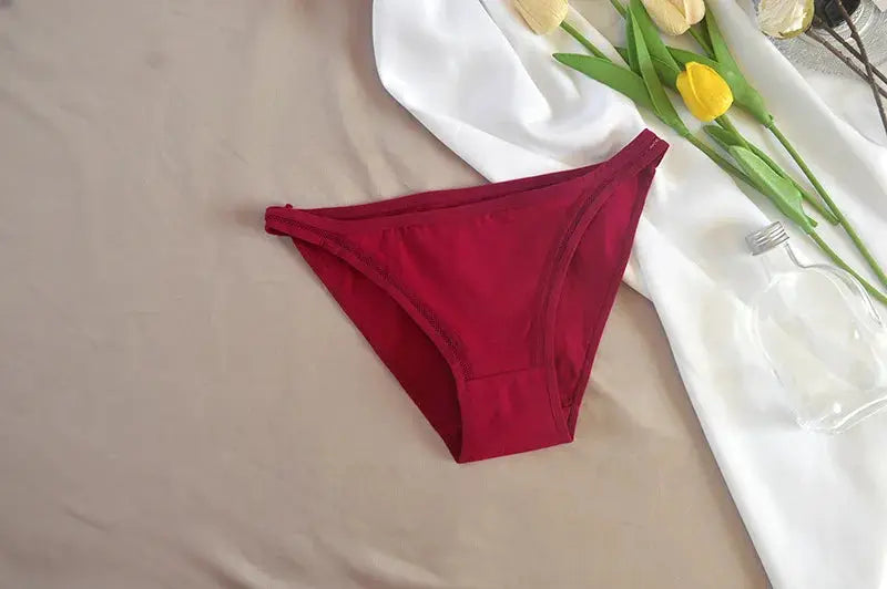 Women's red cotton bikini panties on beige backdrop; solid color underwear.