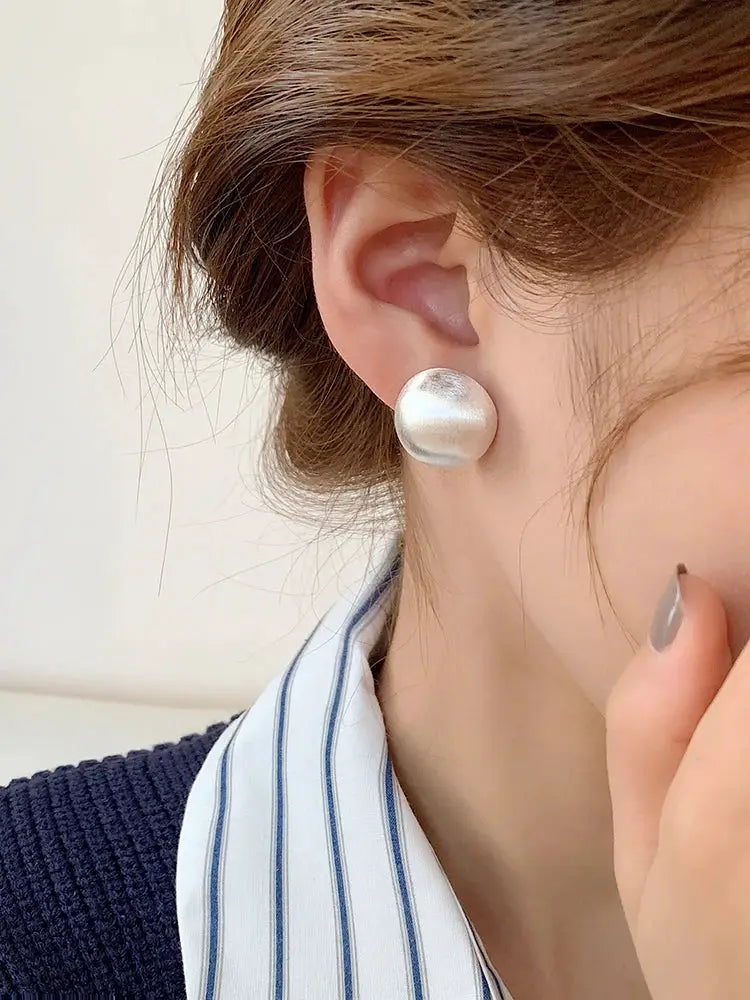 Brushed silver frosted metal stud earring worn on the ear