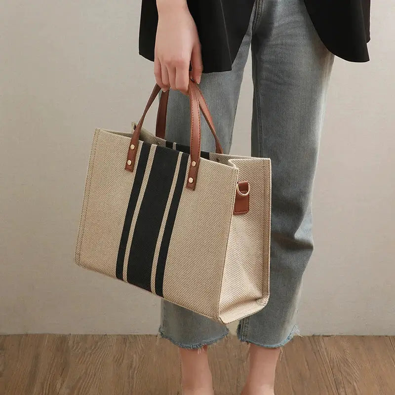 Canvas stripe tote bag with top handles, beige body, black stripe, and brown faux-leather accents for large capacity