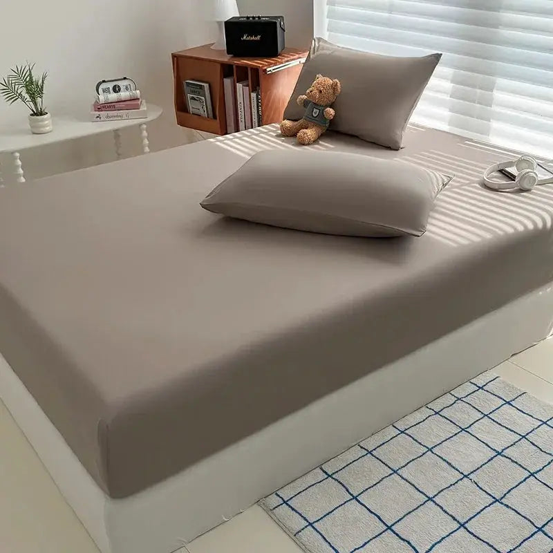 Washed grey fitted sheet with elastic edges on a bed, with pillows; Marshall speaker on shelf