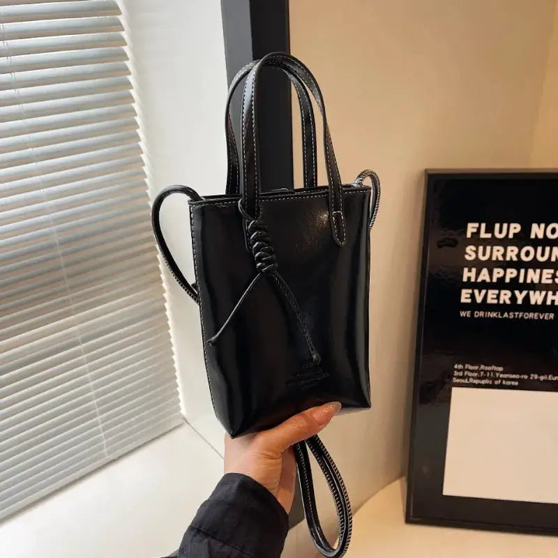 Black PU leather mini crossbody bag with two top handles and a long strap, front tassel knot detail.