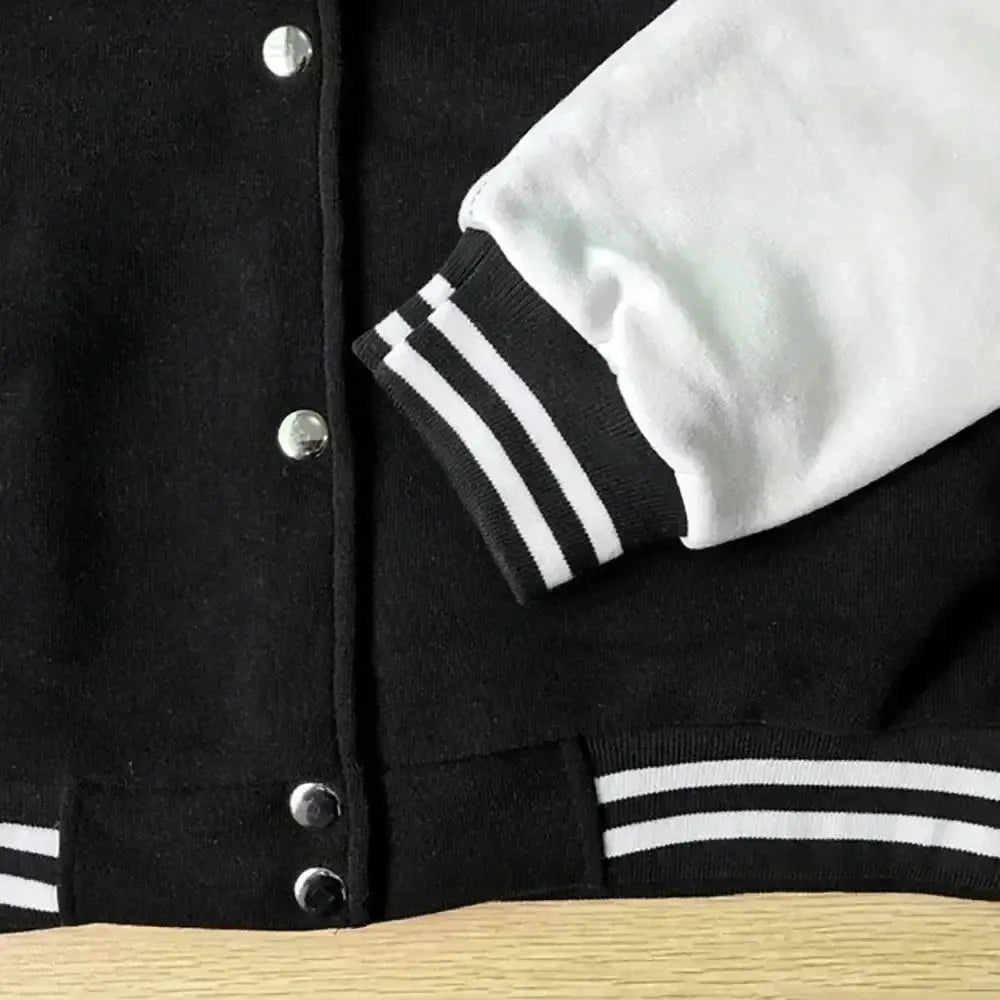 Baseball jacket with black body and white sleeves, striped rib cuffs and hem, metal snap buttons.