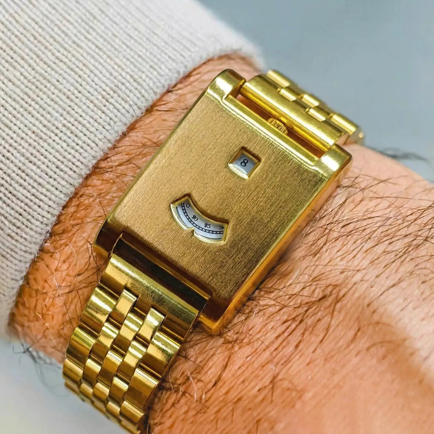 Gold-tone square men's tank watch with brushed finish and linked bracelet; date window shows 8 and power-reserve gauge.