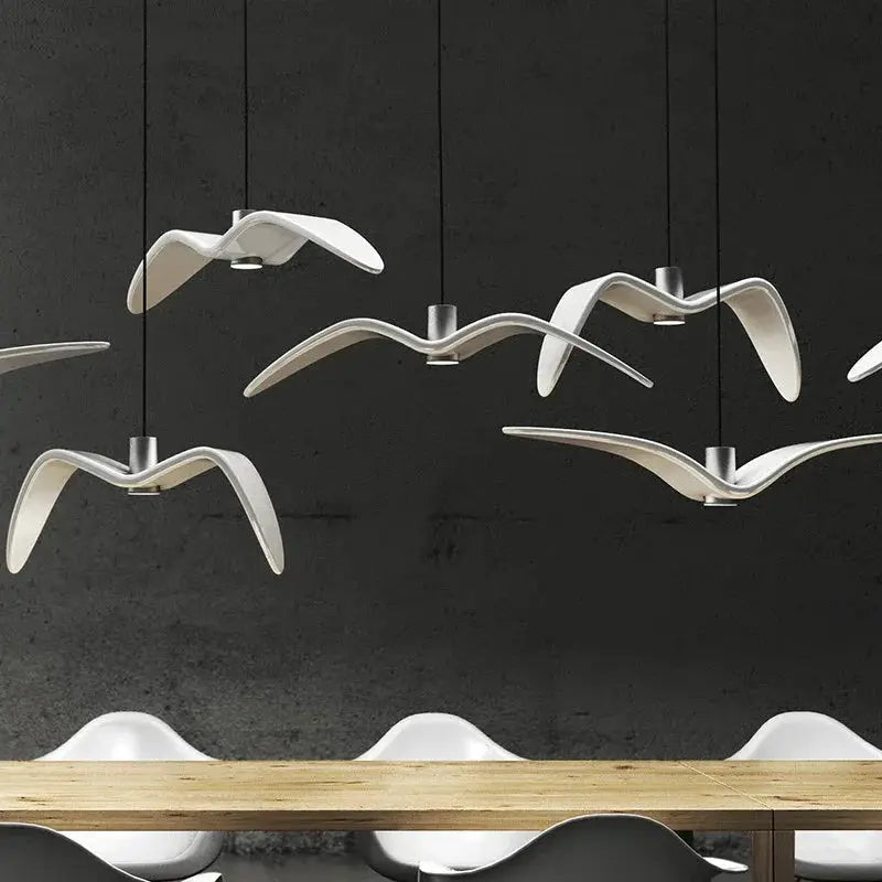 White seagull-shaped LED pendant lamps, modern ceiling luminaires for bar or kitchen, hanging over a wooden dining table