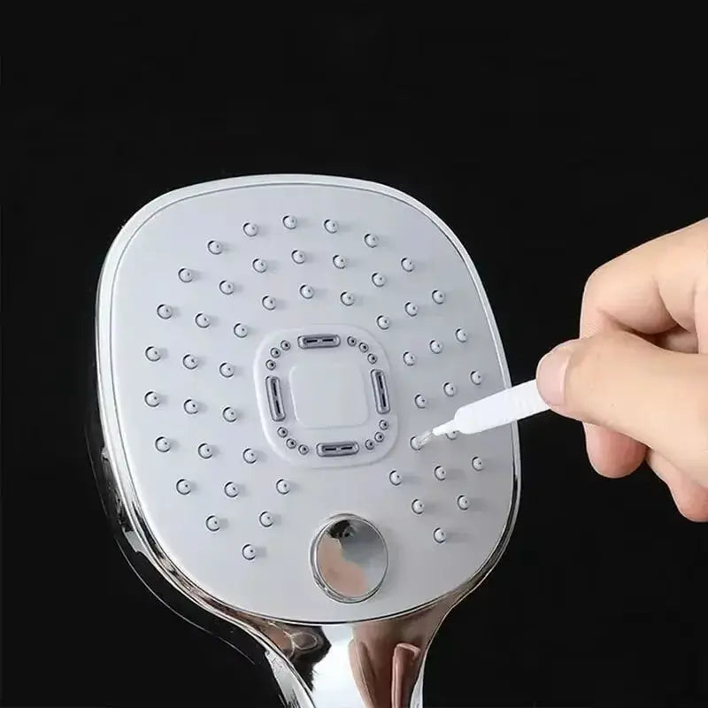 Shower cleaning brush head with micro nylon bristles on a silver square shower plate, hand holding a small cleaning tool