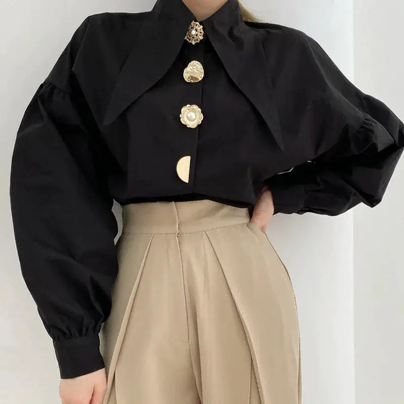 Black puff-sleeve blouse with sharp collar and gold button details, paired with beige high-waisted pleated skirt