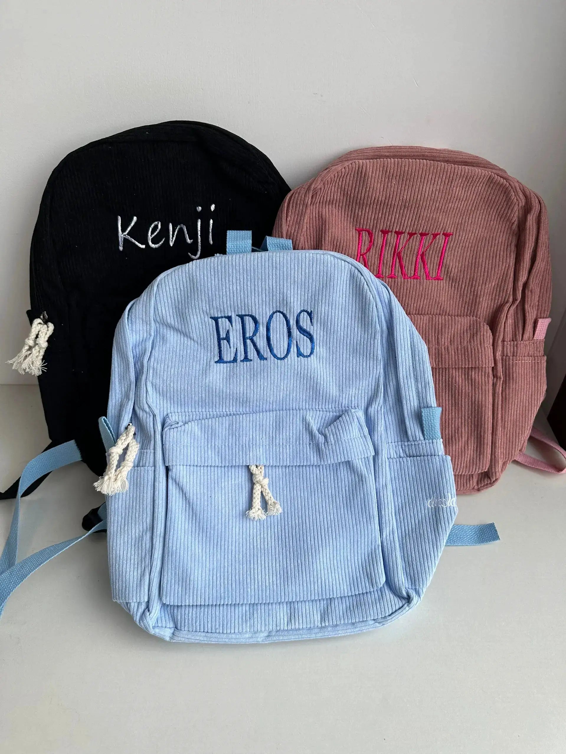 Three personalized kids corduroy backpacks set by Simples Market; black Kenji, blue EROS, pink RIKKI embroidered bags.
