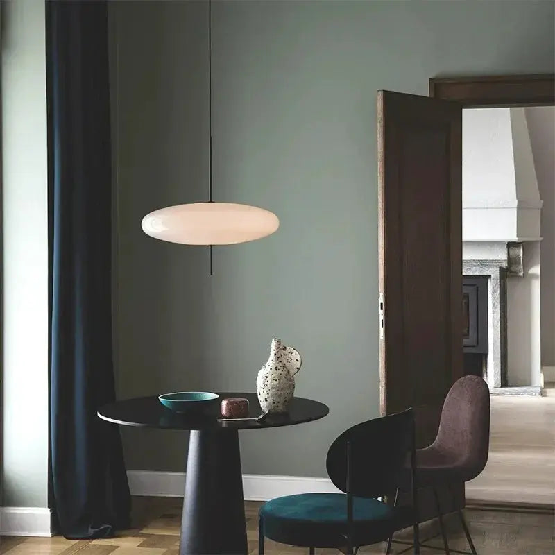 Nordic LED pendant light, white flying-saucer design, hanging over a round black table in a modern living room.