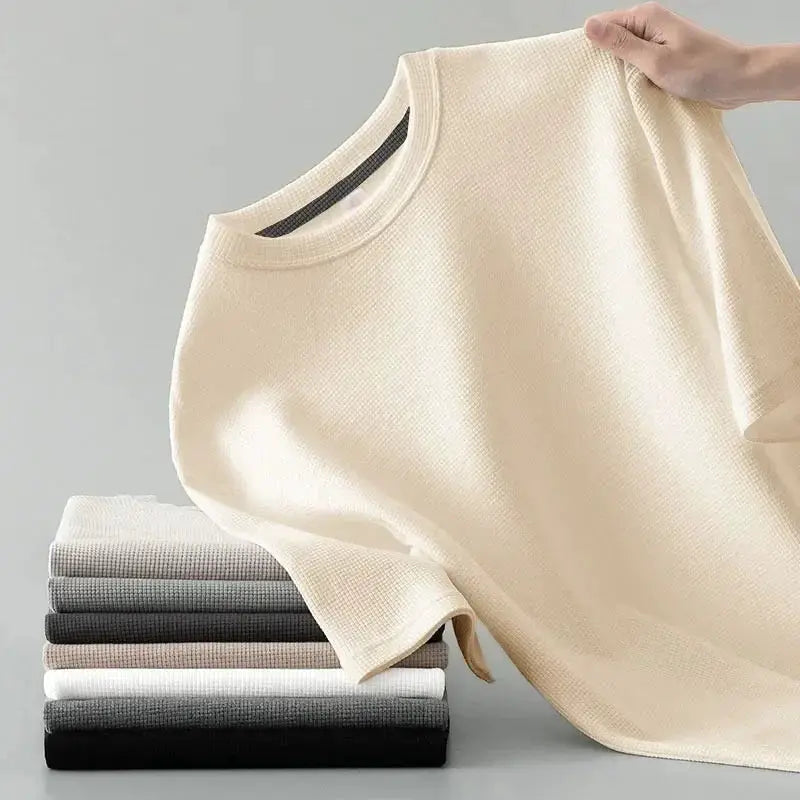 Korean style men's waffle knit T-shirt in beige with short sleeves; stack of folded neutral tees beside.