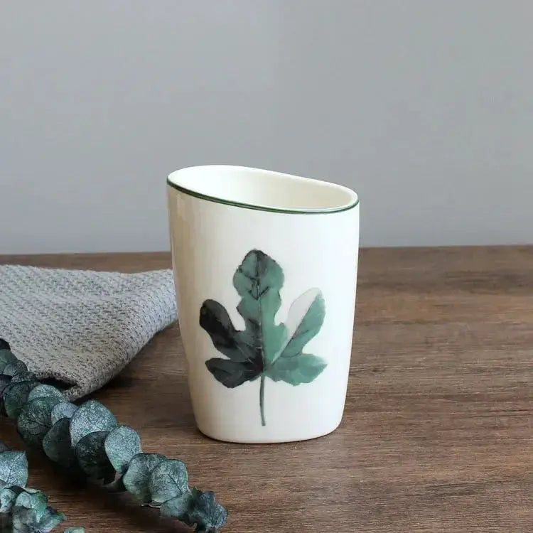 White ceramic bathroom cup with green leaf pattern and green rim
