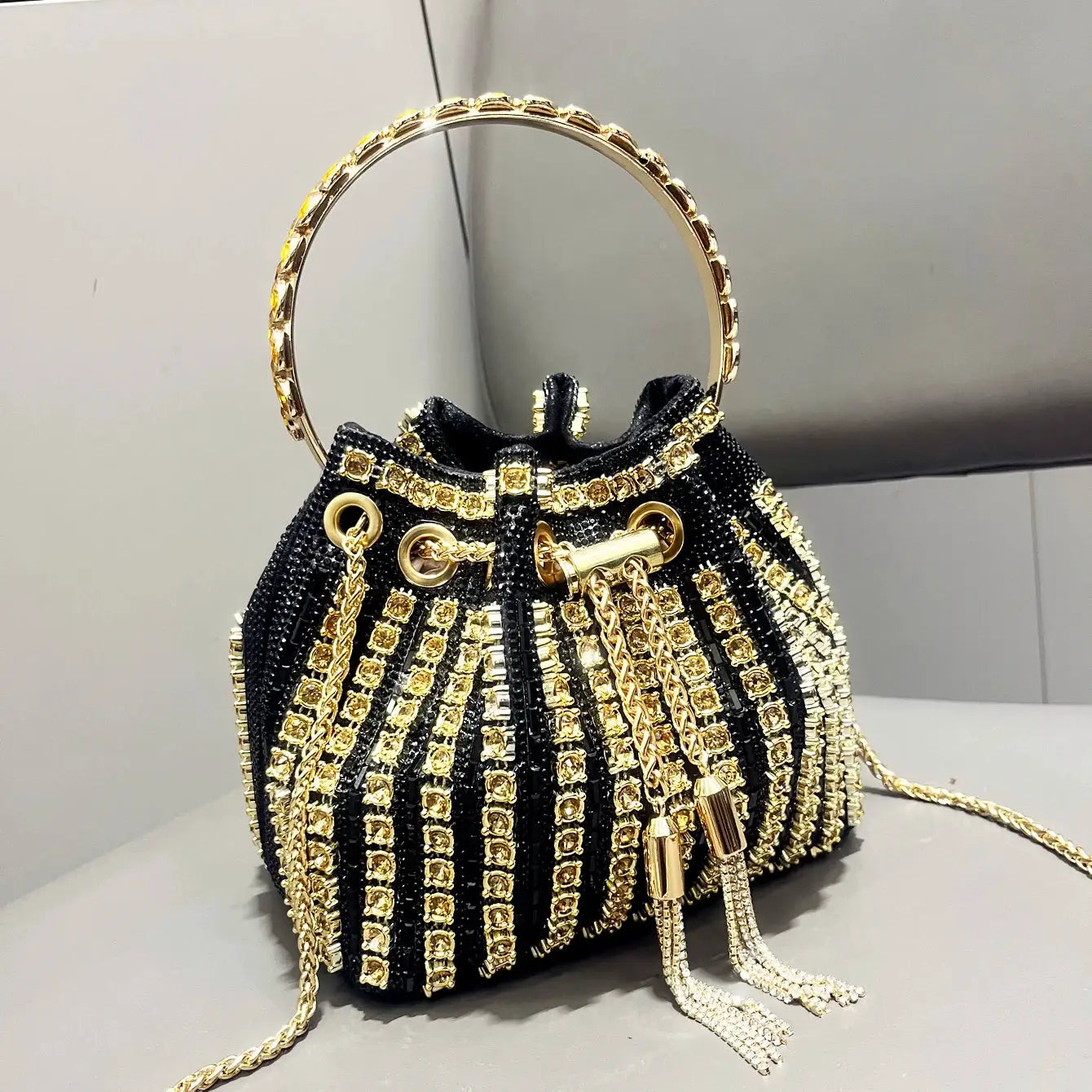 Bucket bag black beaded with gold rhinestone stripes, circular gold handle and tassel chains.