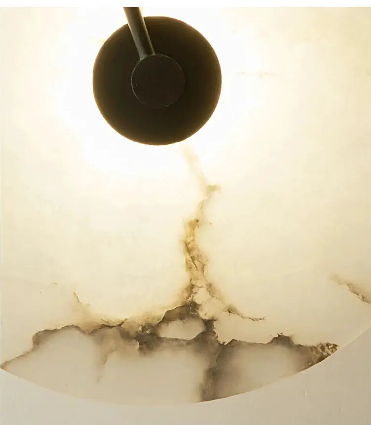 Nordic wall sconce light fixture in black metal with circular head mounted on veined marble wall.