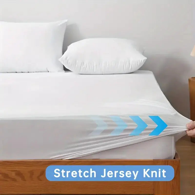 Waterproof mattress protector cover, white stretch jersey knit, pulled taut over a mattress on a wooden bed.