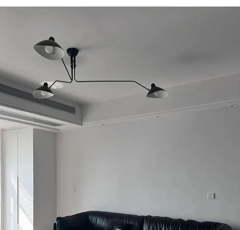 Modern spider pendant light with three black metal shades hangs from the ceiling over a living room sofa.