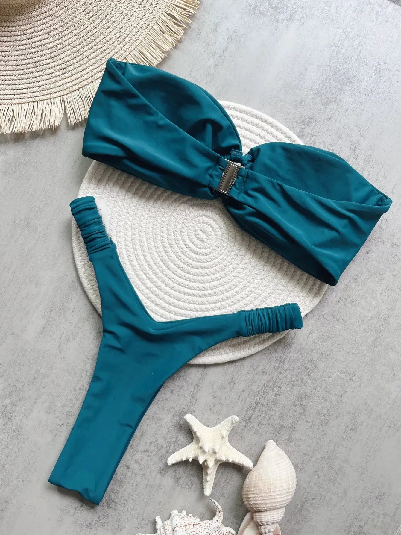 Teal micro bikini set with push-up bandeau top and thong bottoms on a white round mat.