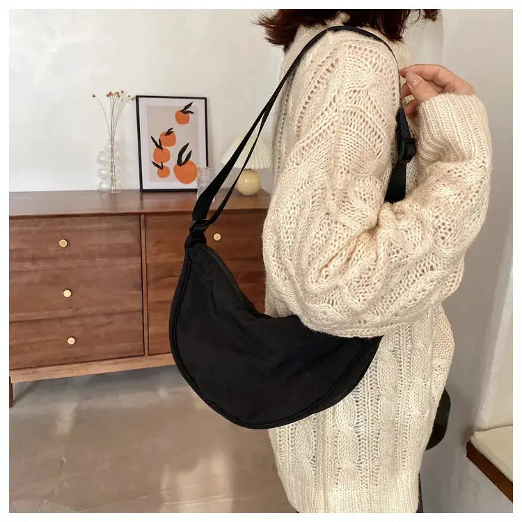 Hobo crossbody bag in black nylon with crescent shape and long adjustable strap.