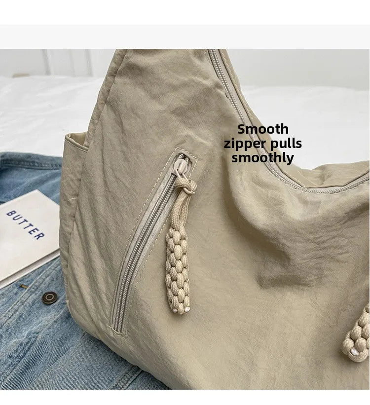 Beige soft-cloth shoulder bag with front zip pocket and knotted zipper pulls.