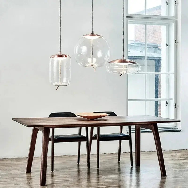 Three minimalist pendant lamps with clear glass globes, copper caps and hemp rope cords