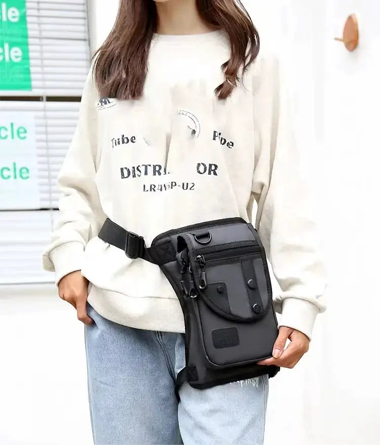 Black leg bag with multiple zip pockets worn at the hip by a woman in a white sweatshirt