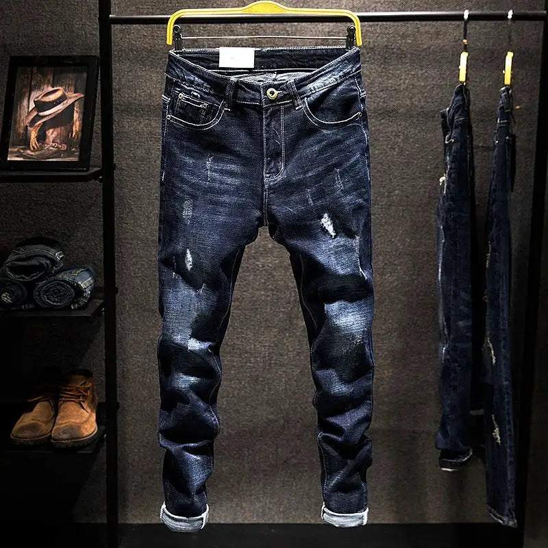 Men's distressed straight jeans in dark blue cotton denim with ripped patches.