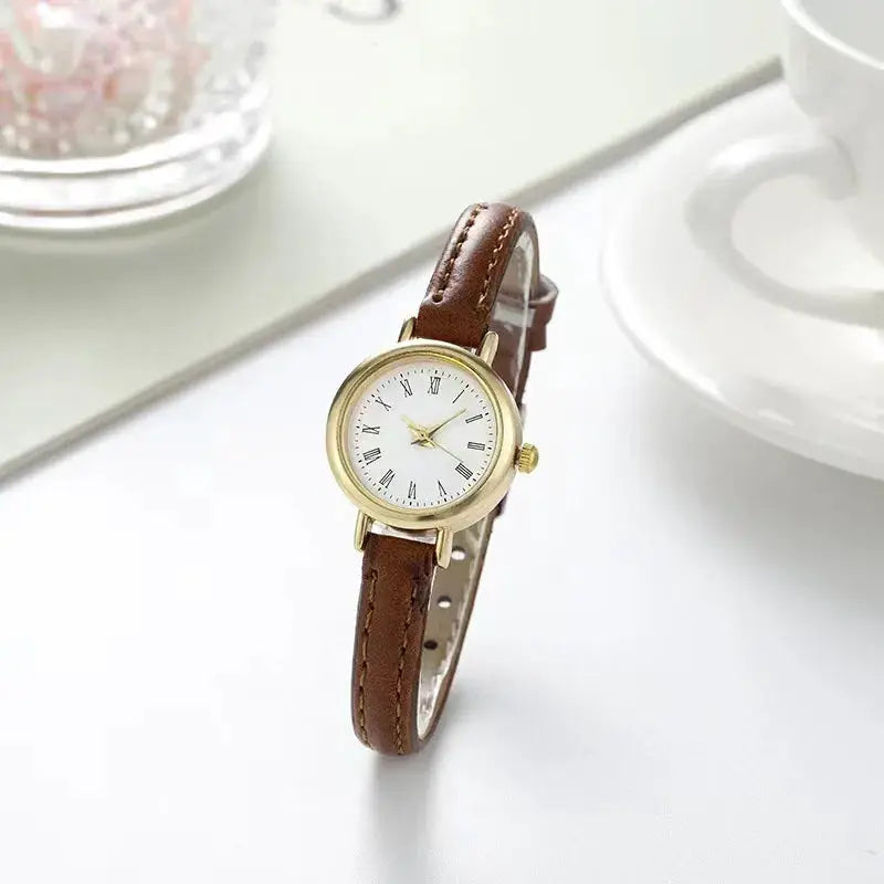 Women's brown leather band quartz watch by Simples Market with gold-tone case and Roman numeral dial.