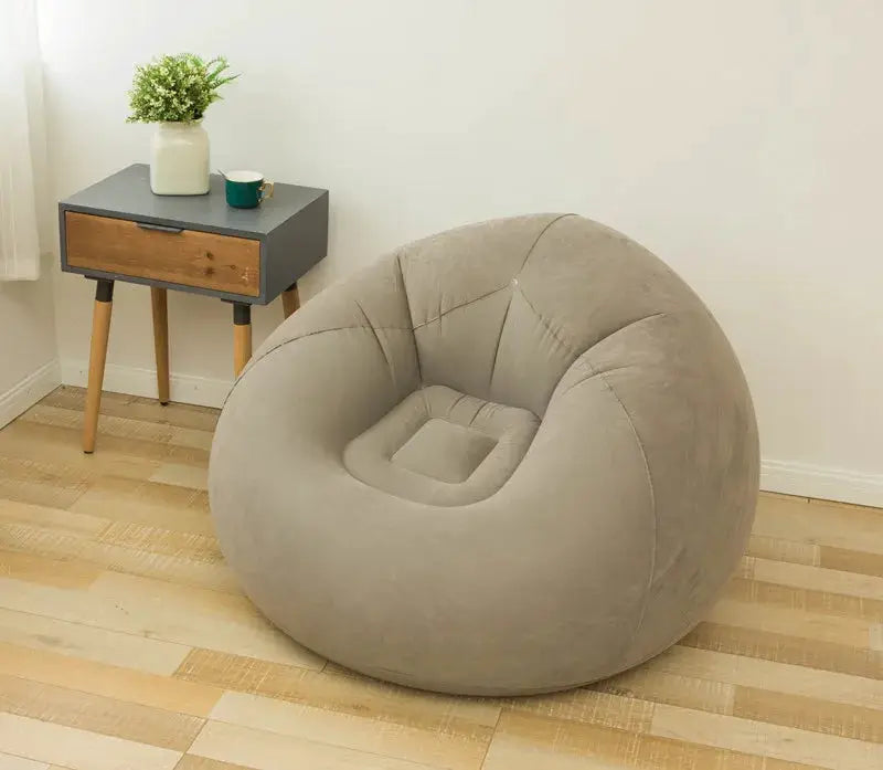 Large gray inflatable sofa chair PVC lounger in a living room with a wooden side table, plant, and mug on top.